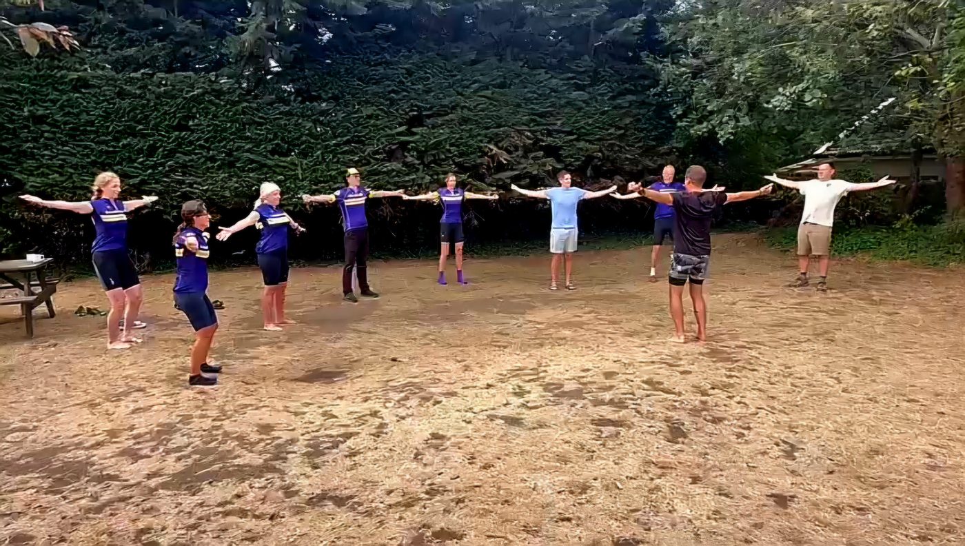 A group practising Qigong outdoors, standing in a line with arms outstretched